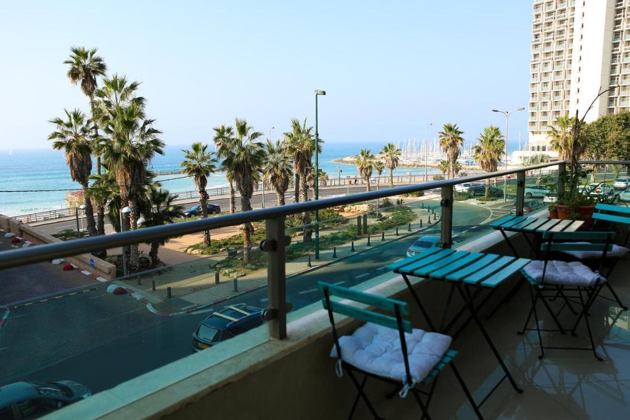 Balcony with a table and chairs facing the sea, with HaYarkon Street below